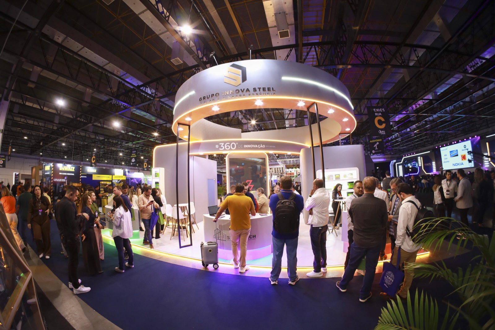 Estande circular do Grupo Innova Steel no ENICS, com visitantes em volta do balcão iluminado