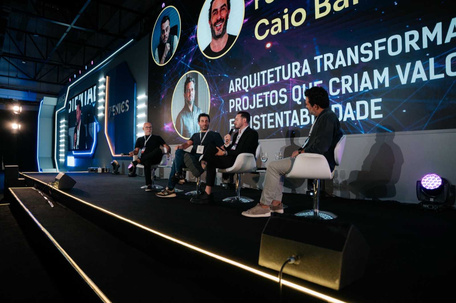 Mesa redonda no palco do ENICS, com quatro participantes e telão ao fundo